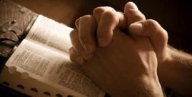 Hands joined in prayer over an open Bible